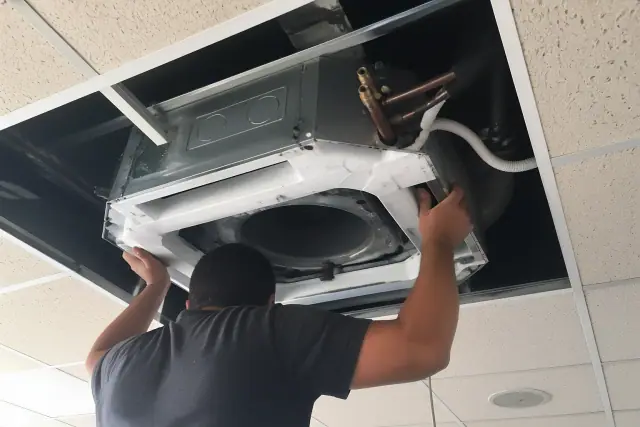 Technician installing a ceiling-cassette VRF unit into a drop ceiling at a job site in Gilbert, AZ.