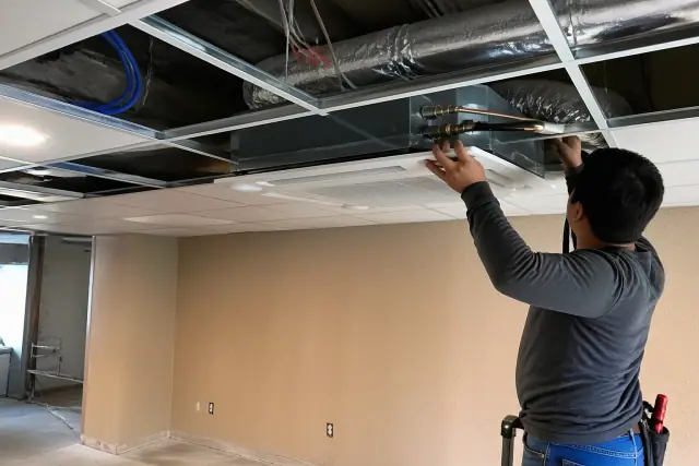 Technician installing a ceiling-cassette VRF indoor unit into a drop ceiling in Goodyear, AZ.