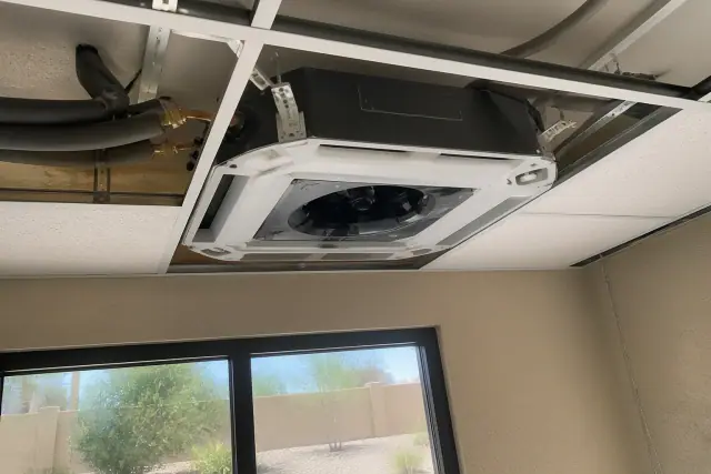 Technician installing a ceiling-cassette VRF indoor unit in a Tempe, AZ office with visible copper refrigerant lines.