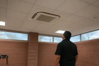 Technician inspecting a flush-mounted VRF ceiling unit near terracotta walls and clerestory windows in Phoenix, AZ.