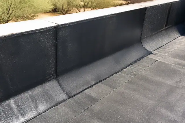 APP torch-applied membrane seam on a parapet wall in Phoenix, AZ, showing a fused bitumen edge with desert brush nearby.