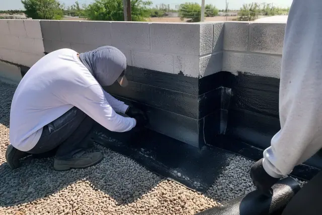 Contractors sealing a parapet wall with bitumen felt on a gravel flat roof in Phoenix, AZ.