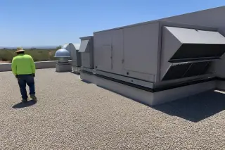 Worker inspecting a finished built-up roof with gravel ballast and an HVAC unit in Phoenix, AZ.