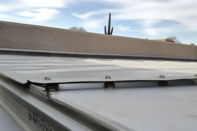Industrial screws fastening metal roof panels on a commercial building in Phoenix, AZ, with a saguaro cactus in the distance.