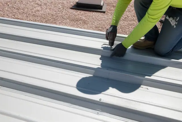 Technicians fastening metal roofing panels with industrial screws and sealant on a building roof in Phoenix, AZ.