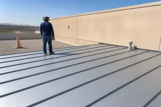 Professional inspecting finished metal roof panels next to an orange safety cone and stucco wall in Phoenix, AZ.