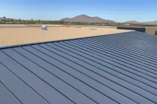 Overlapping metal roofing sheets with industrial screws near tan gravel ballast and desert mountains in Phoenix, AZ.