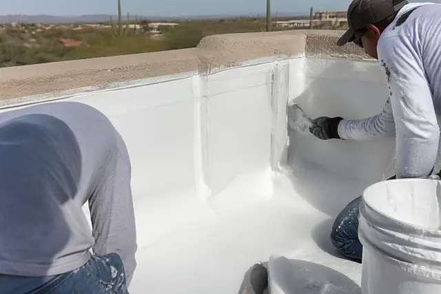 Crew applying white elastomeric roof coating to a parapet wall flashing at a jobsite in Phoenix, AZ.