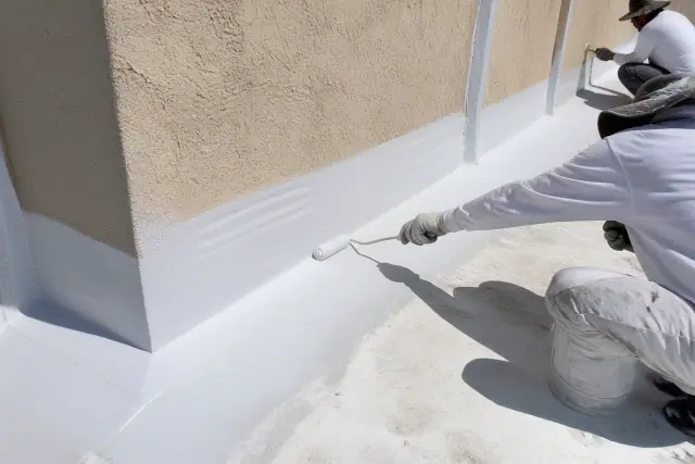 Worker applying a commercial roof coating to a parapet wall at a jobsite in Phoenix, AZ.