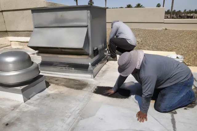 Technicians performing a commercial roof inspection near a ventilation unit in Tempe, AZ.