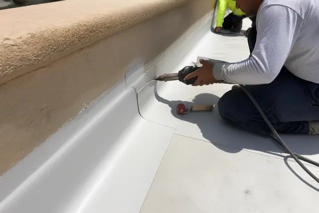 Roofing crew heat-welding TPO membrane seams on a stucco parapet wall during a commercial project in Chandler, AZ.