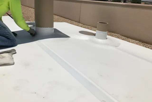 Technicians heat-welding TPO membrane seams around a rooftop unit in Phoenix, AZ with gravel and a stucco wall nearby.