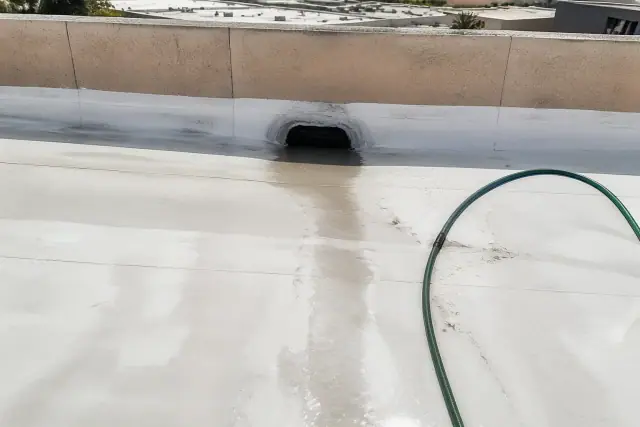 Wet drainage scupper and debris grate on a white commercial roof in Phoenix, AZ.