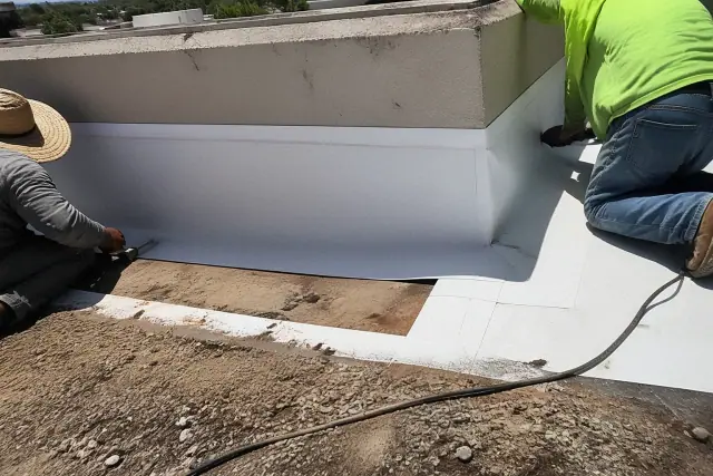 Crew members sealing TPO roofing membrane seams at a parapet wall during a full roof replacement in Phoenix, AZ.