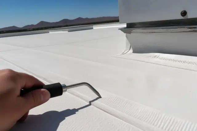 Technician testing a heat-welded TPO roof seam with a probe tool on a sunny day in Phoenix, AZ.