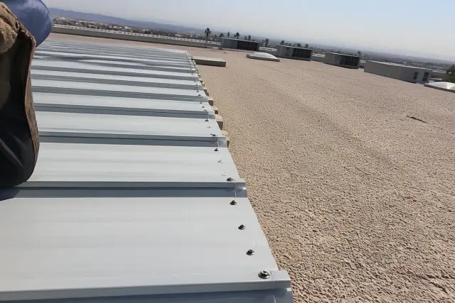 Technician installing industrial screws along a metal roofing seam on a sunny rooftop in Phoenix, AZ.