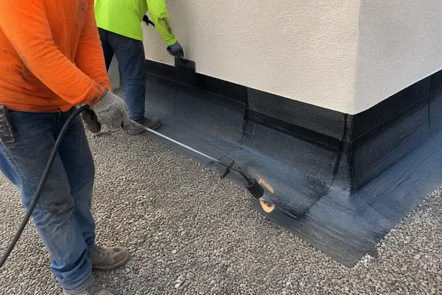 Roofing contractors sealing bitumen membrane joints along a parapet wall on a building in Phoenix, AZ.