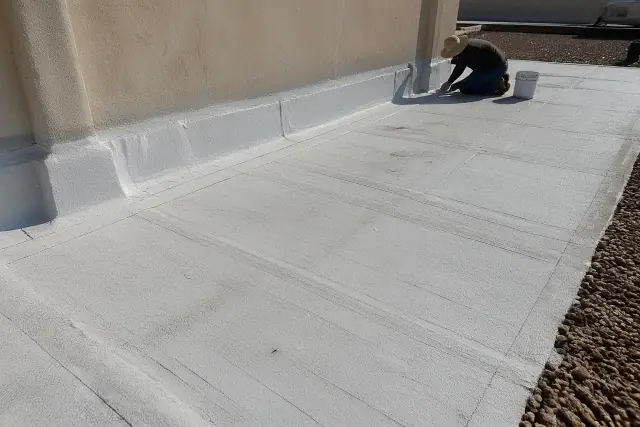 Reflective white-coated built-up roofing layers with bitumen seams near a gravel border on a rooftop in Phoenix, AZ.
