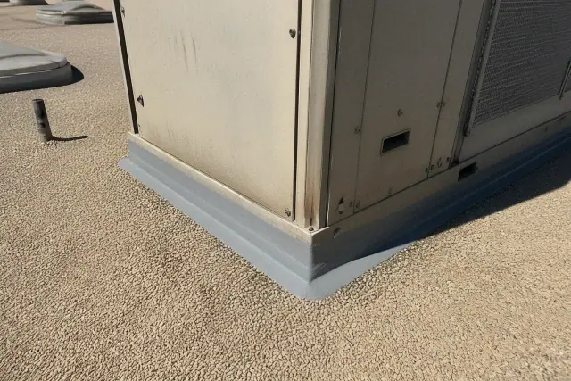 Technician applying grey sealant around a rooftop HVAC unit on a gravel roof in Phoenix, AZ.