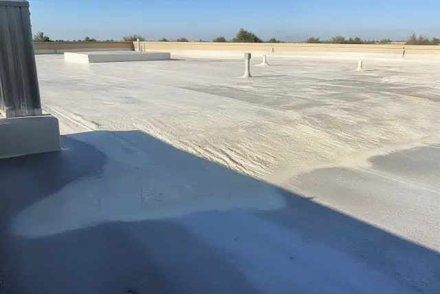 Spray foam roof repair and recoating on a commercial flat roof in Phoenix, AZ under bright sunlight.