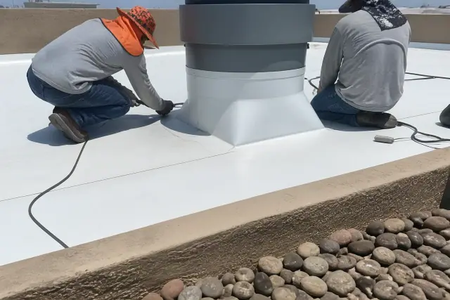 TPO roofing membrane with heat-welded seams on a commercial roof in Gilbert, AZ, framed by river rock and a stucco parapet.
