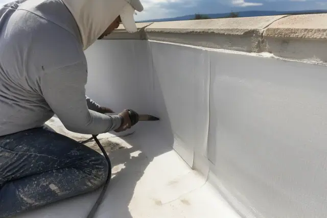 Technician heat-welding white TPO roofing membrane along a parapet wall corner at a job site in Phoenix, AZ.