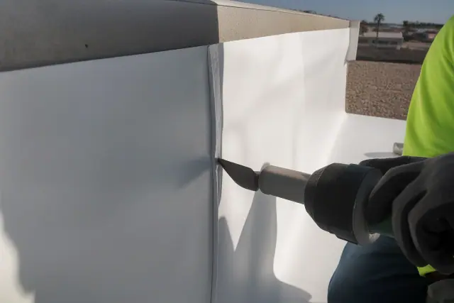 Roofing crew using a heat welder to seal TPO membrane seams on a parapet wall at a job site in Phoenix, AZ.