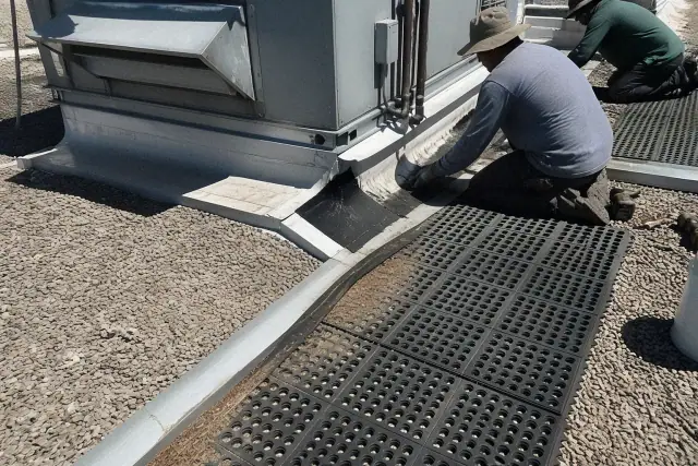 Technicians performing rooftop membrane detailing near an HVAC unit in Phoenix, AZ, with walkway mats and debris.