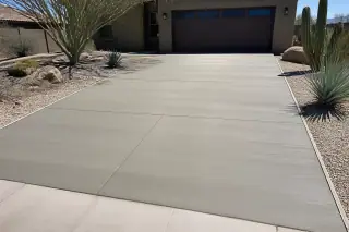 A finished concrete driveway with a uniform broom-brushed texture and desert landscaping in Phoenix, AZ.