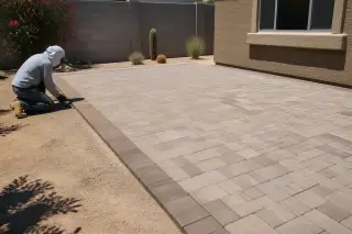Technician cleaning the edges of an interlocking concrete paver patio with desert landscaping in Phoenix, AZ.