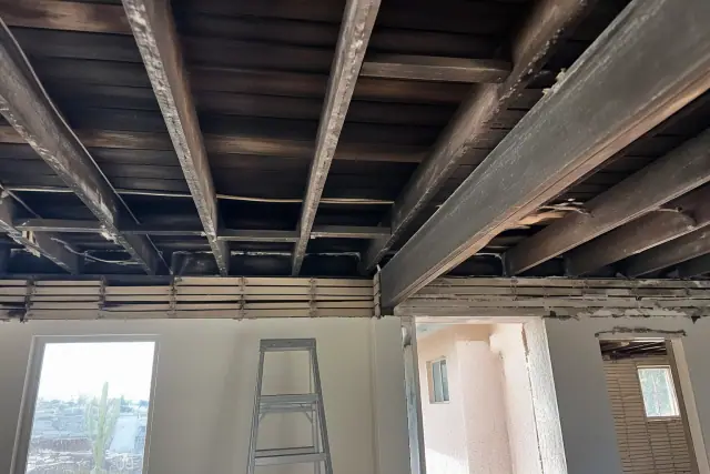 Exposed structural ceiling beams and framing viewed from a ladder at a jobsite in Phoenix, AZ.