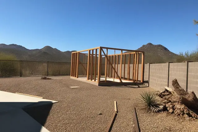 Skeletal wooden frame of a demolished outbuilding on a gravel lot in Phoenix, AZ.