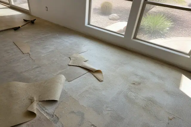 Torn vinyl flooring being removed from a subfloor in a residential home in Goodyear, AZ.