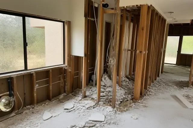 Interior gut demolition progress in a Phoenix, AZ home showing exposed wall framing, debris, and dangling wiring.