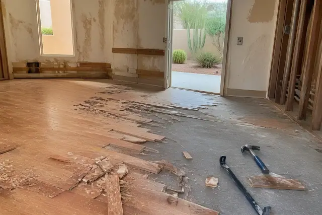 Hardwood flooring removal in progress with pry bars on an exposed subfloor in a Phoenix, AZ home.