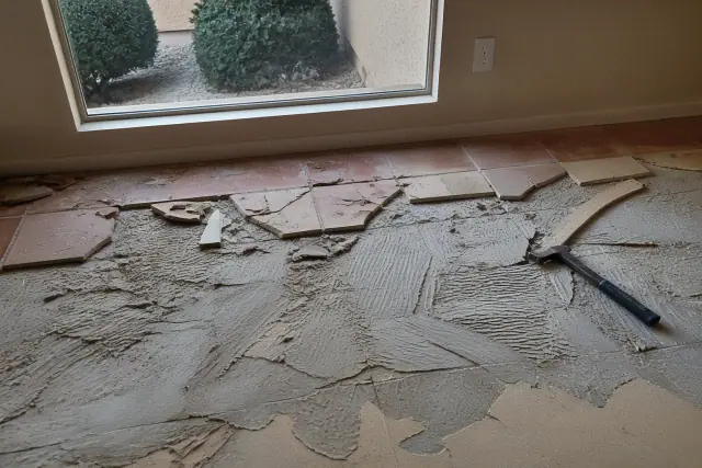 Natural stone and saltillo tiles being pried from a residential subfloor during a renovation in Phoenix, AZ.