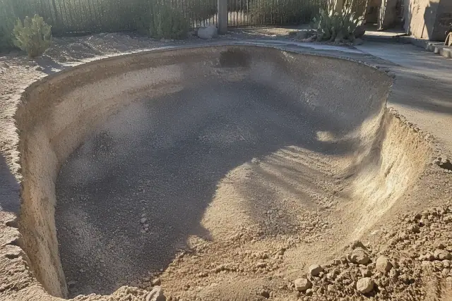 Excavated residential pool site filled with aggregate in Scottsdale, AZ, surrounded by desert landscaping.