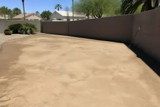 Leveled and compacted soil in a Phoenix, AZ backyard with a rake leaning against a fence.