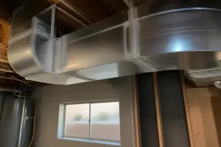 Off-white sealant at silver metal ductwork seams visible through a basement window in Phoenix, AZ.
