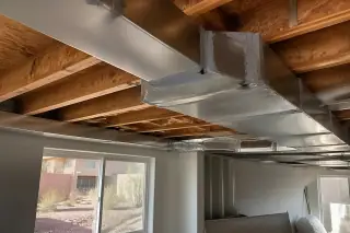 Sealed silver metal ductwork joints in an unfinished basement with a view of xeriscape landscaping in Phoenix, AZ.