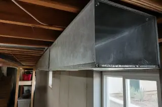 Sanitized metal air ducts with visible brush marks between exposed wood joists in a Phoenix, AZ basement.