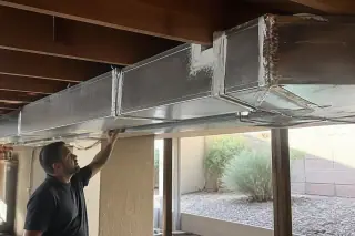 Mastic-sealed metal air duct seams and floor joists in a Phoenix, AZ basement with desert landscaping outside.