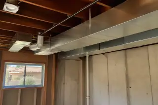 Exposed silver metal ductwork and open floor joists in an unfinished Phoenix, AZ basement.