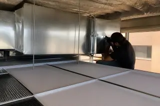 Technician inspecting clean galvanized steel ventilation trunks above a suspended ceiling in Phoenix, AZ.
