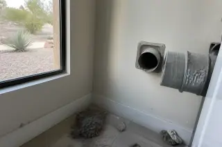 Disconnected dryer exhaust pipe showing cleaned lint buildup in a Phoenix, AZ laundry room with a window view.