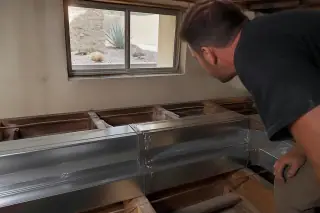 Cleaned silver metal air ducts and exposed wooden joists viewed through a basement window in Phoenix, AZ.