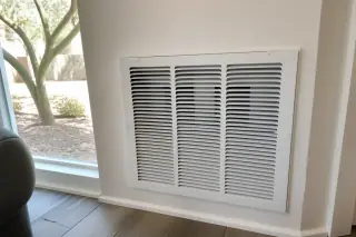 Clean return-air grille on a wall with desert xeriscape and a palo verde tree visible through a window in Phoenix, AZ.