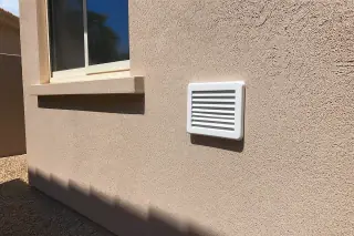 Reinstalled white wall-mounted vent cover on a stucco wall in a Phoenix, AZ home.