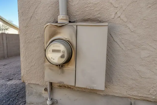 Heat-damaged electrical meter box with thermal discoloration on an exterior stucco wall in Phoenix, AZ.