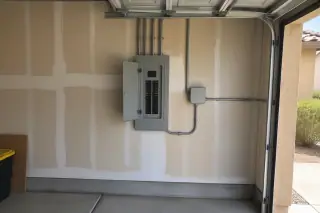 Wide view of a breaker enclosure and conduit on a garage wall in Phoenix, AZ.